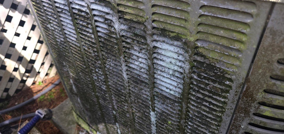 Dirty outdoor AC condenser coil showing buildup before cleaning