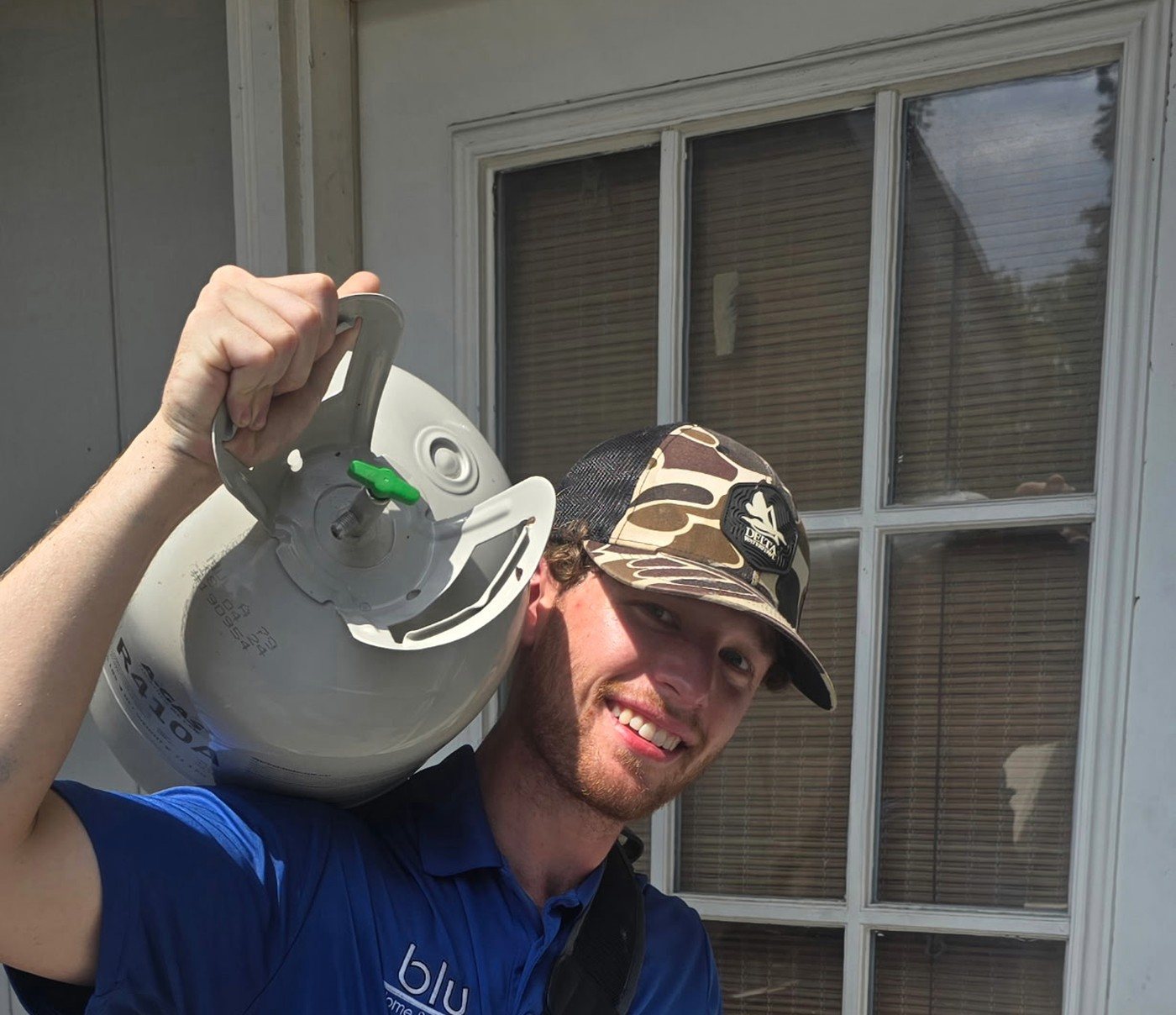 Smiling BLU Home Services HVAC technician arriving at a customer home with refrigerant tank and tool bag
